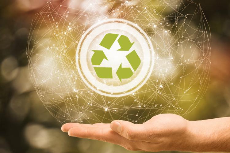 Tecnologia e meio ambiente: mão aberta sob um fundo com tons predominantemente verdes, e acima dela uma forma circular. Dentro dessa forma está o símbolo da reciclagem.